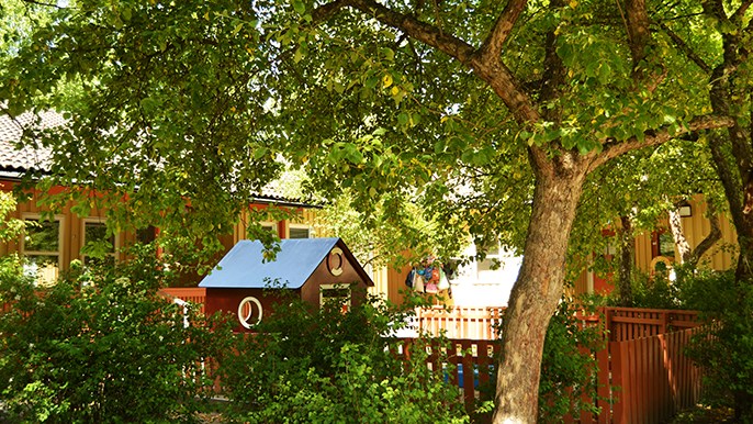 Bild av en lekplats och träd framför förskolan Trädgården