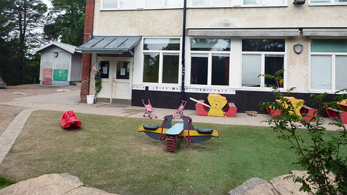 En mindre förskolegård med gräsmatta, leksaker och buskar.