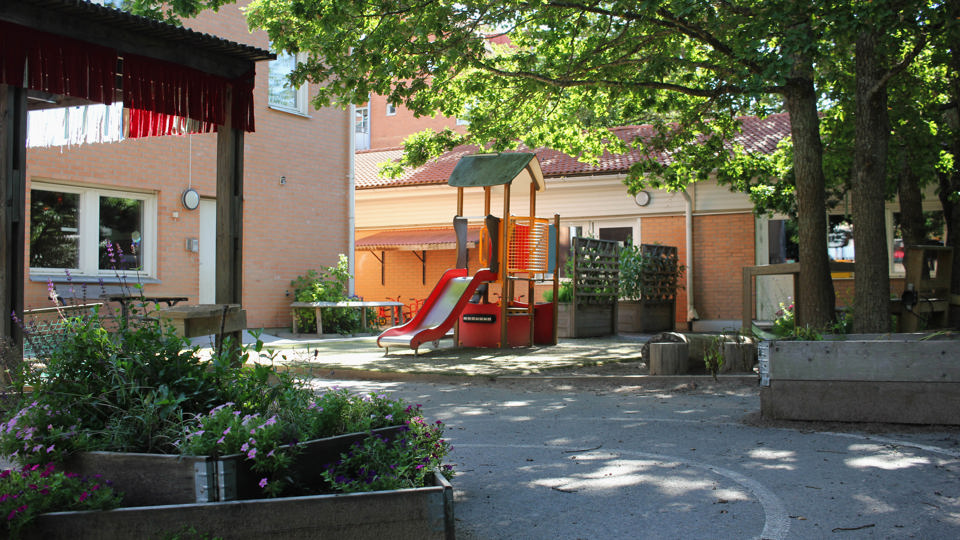 Förskolan Skogsgläntans utegård med klätterställning i gult och rött, planteringslåda med blommor i.