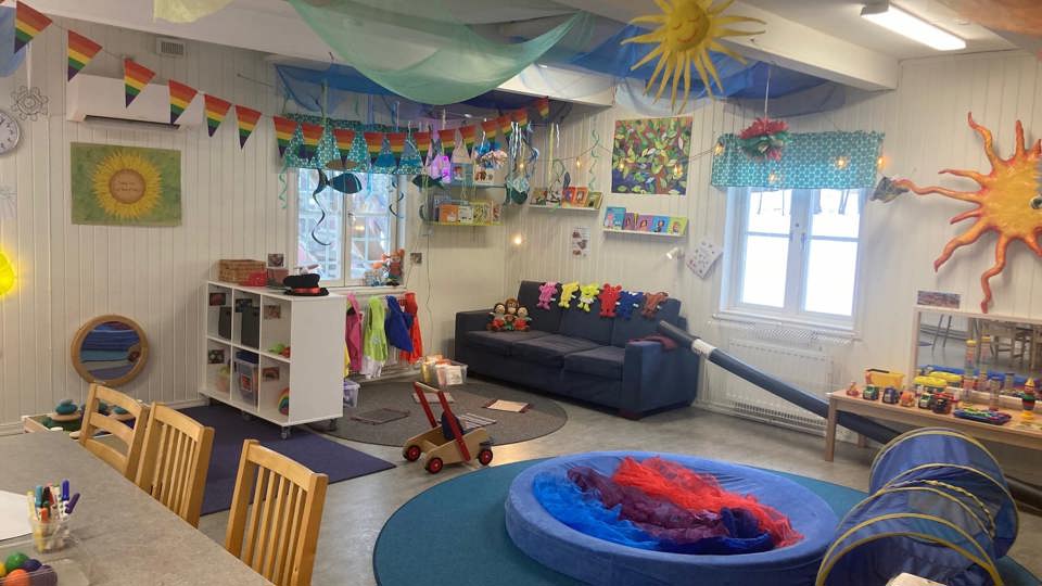 Ett lekrum i en öppen förskola med soffor, mattor, leksaker, böcker och färgglada dekorationer.