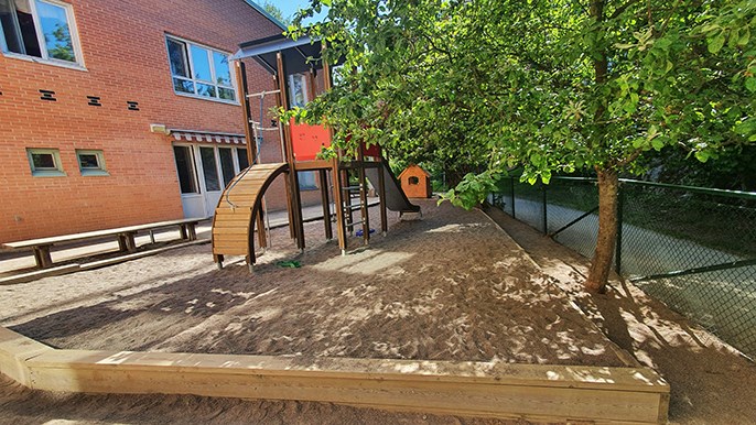 Bild av sandlåda, klätterställning och träd utanför förskolan Kryddgården