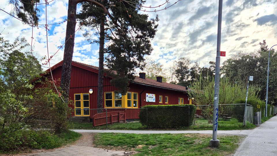 Röd-gul träbyggnad omgivet av grönska, foto.