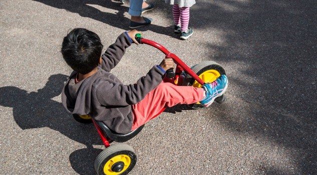 Barn cyklar på en trehjuling ute på gården.