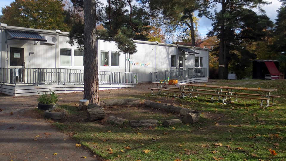 Del av förskolegården med gräsmatta och förskolehuset i bakgrunden.
