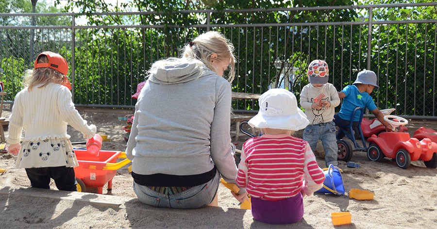 Barn och vuxen leker i sandlåda med leksaker.