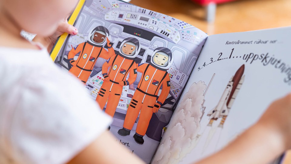 Ett barn som läser en bok som visar en bild på tre austronauter