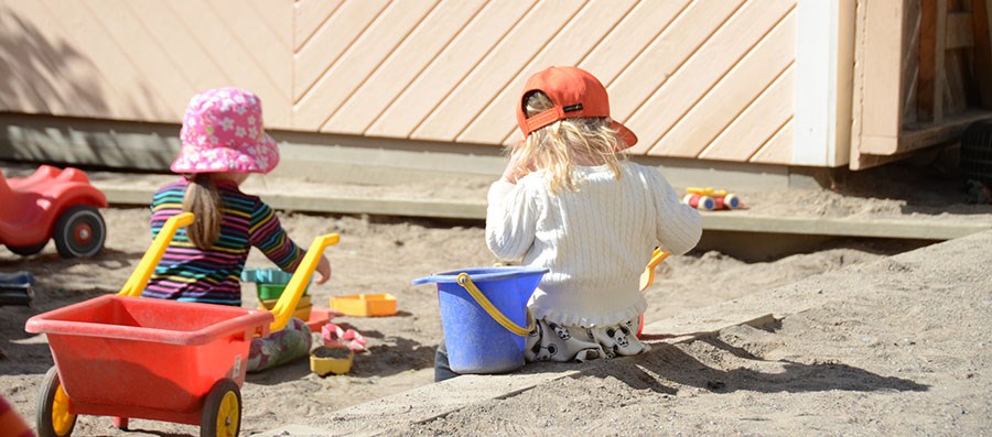 Barn leker i sandlåda med leksaker på förskolans utegård.