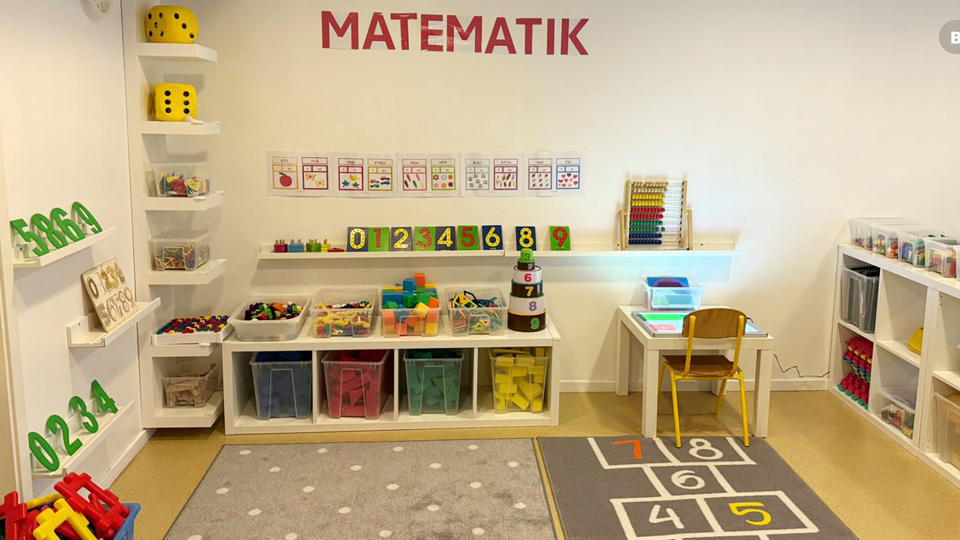 En hörna med lekmaterial - bokstäver och siffror, tärningar och hyllor med färgglada leksaker.