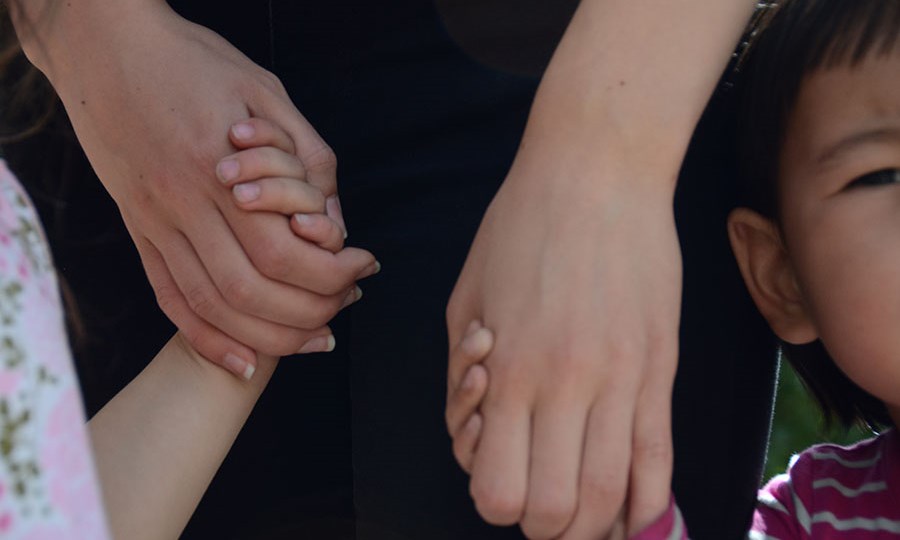 Barn och vuxna håller i varandras händer på förskolans utegård.