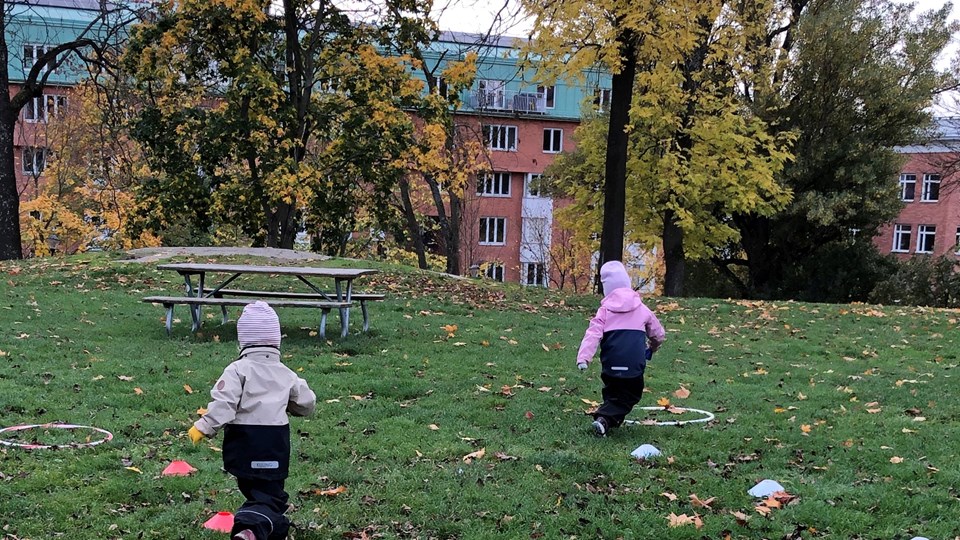 Två barn springer på gräsmatta.