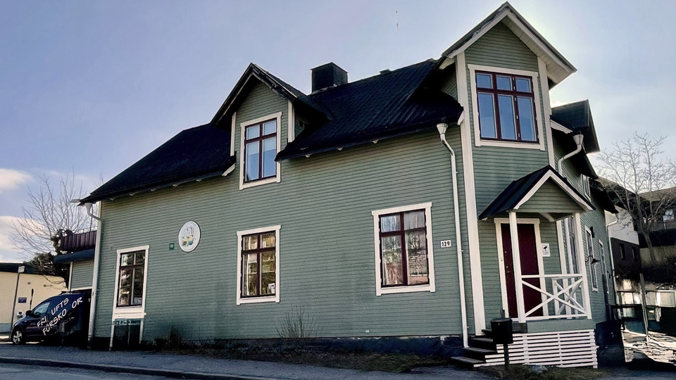 Grönmålat trähus invid en gata. 